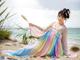 A woman in a colorful dress sitting on a beach.