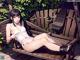 A woman sitting on a wooden bench in a white bikini.