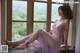 A woman in a pink dress sitting on a window sill.