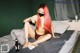 A woman with red hair sitting on a bed with a bottle of beer.